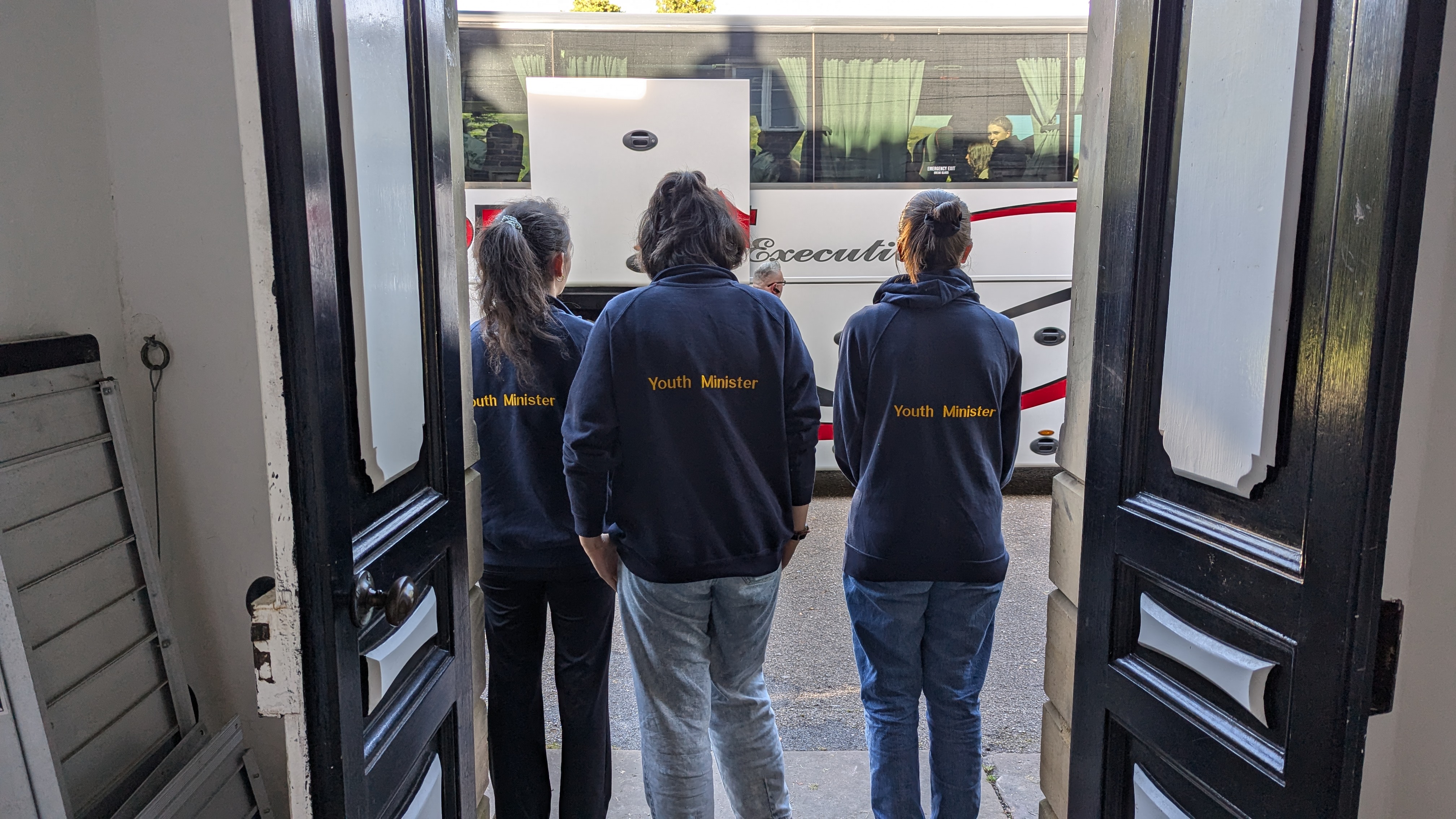 Three Castlerigg Youth Ministers in branded hoodies welcoming a group off the coach